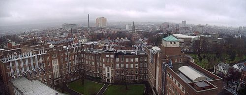 View of Belfast from Queens University Ashby Building. The main Laynon Building of Queen's University is in the foreground. The yellow fasciad Belfast City Hospital is visible in the center background, with the city's current tallest building Windsor House in the right background.