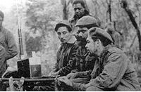 Listening to a shortwave radio are (seated from the left) Rogelio Oliva, José María Martínez Tamayo (known as "Mbili" in the Congo and "Ricardo" in Bolivia), and Guevara. Standing behind them is Roberto Sánchez ("Lawton" in Cuba and "Changa" in the Congo).