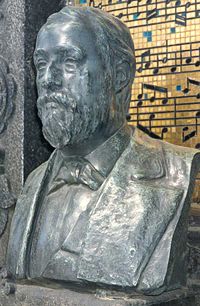 The bust of Borodin at his tomb in Tikhvin Cemetery(The visible musical notation on the tile monument in the background shows themes from "Gliding Dance of the Maidens" from Polovetsian Dances; "Song of the Dark Forest"; and the "Scherzo" theme from Symphony No. 3)