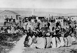 "Shoshone Indians at Ft. Washakie, Wyoming Indian reservation. Chief Washakie (at left) extends his right arm." Some of the Shoshones are dancing as the soldiers look on.