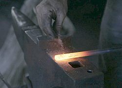A blacksmith removes rust with sand prior to welding.