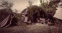 Chiricahua medicine man in wickiup with family