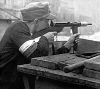 Polish insurgent, wearing armband in the national colors, at a Warsaw Uprising barricade. He is using the Polish submachine gun Błyskawica.