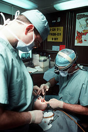 A dentist and dental assistant perform surgery on a patient.