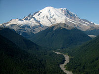 Mount Rainier with its main summit, Columbia Crest (14,410 feet) at the center. Massive Emmons Glacier covers most of the visible flank of the mountain. Left of the glacier is sharp pointed Little Tahoma (11,138 feet) with Frying Pan Glacier on its flank.