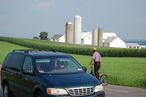 Amish man pedals his bike while a mini-van speeds past