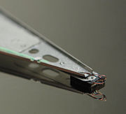 Close-up of a hard disk head suspended above the disk platter together with its mirror image in the smooth surface of the magnetic platter.