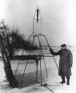 Robert Goddard, bundled against the cold New England weather of March 16, 1926, holds the launching frame of his most notable invention — the first liquid-fueled rocket.