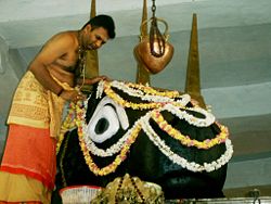 Hindu priest placing garlands of fresh flowers on the head of a massive statue of the god Shiva's bull Nandi.