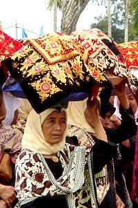 Women carrying covered platters of food to a ceremony