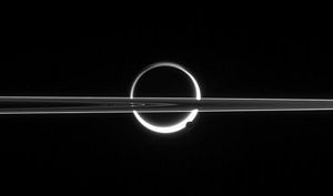 Saturn's rings cut across an eerie scene that is ruled by Titan's luminous crescent and globe-encircling haze, broken by the small moon Enceladus, whose icy jets are dimly visible at its south pole. North is up.