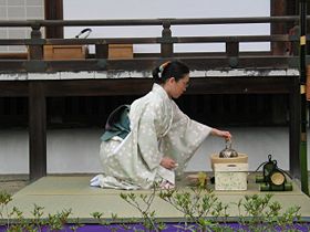 A woman wearing kimono performs a tea ceremony seated in seiza osition on tatami