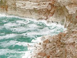 A rough Dead Sea, with salt deposits on cliffs.