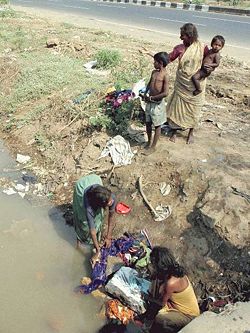 Poverty-stricken women washing clothes by a road in Mumbai, India.