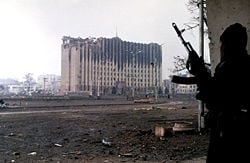 A Chechen fighter near the burned-out ruins of the Presidential Palace in Grozny, January 1995. Photo by Mikhail Evstafiev