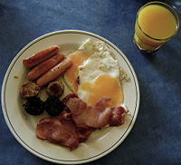 An Irish breakfast consisting of sausages, black and white pudding, bacon, and fried eggs, served with a glass of orange juice.