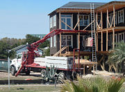 Drywall is delivered to a building site on a flatbed truck and unloaded with a forked material handler crane. The bulk drywall sheets are unloaded directly to upper floors via a window or exterior doorway.
