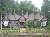 Rumah gadang in the Pandai Sikek village of West Sumatra, with two rice barns (rangkiang) in front.